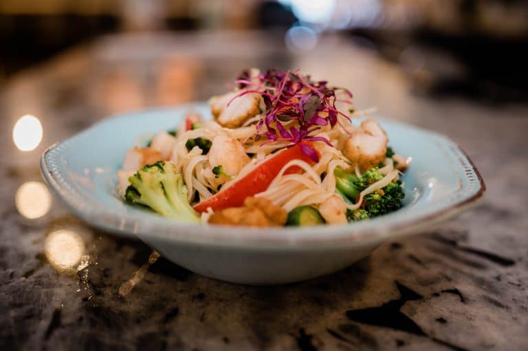 A bowl of mixed vegetable and seafood salad on a marble surface, garnished with shredded purple cabbage.