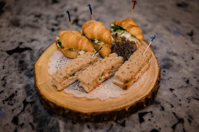 An assortment of croissant and sandwich finger foods on a wooden platter, garnished with green leaves and held together with toothpicks.