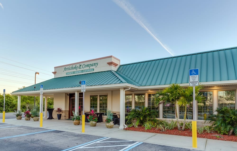 A single-story building with a green roof houses Artichoke & Company, offering events, dining, and catering services. There are accessible parking spaces and planters with greenery at the entrance.